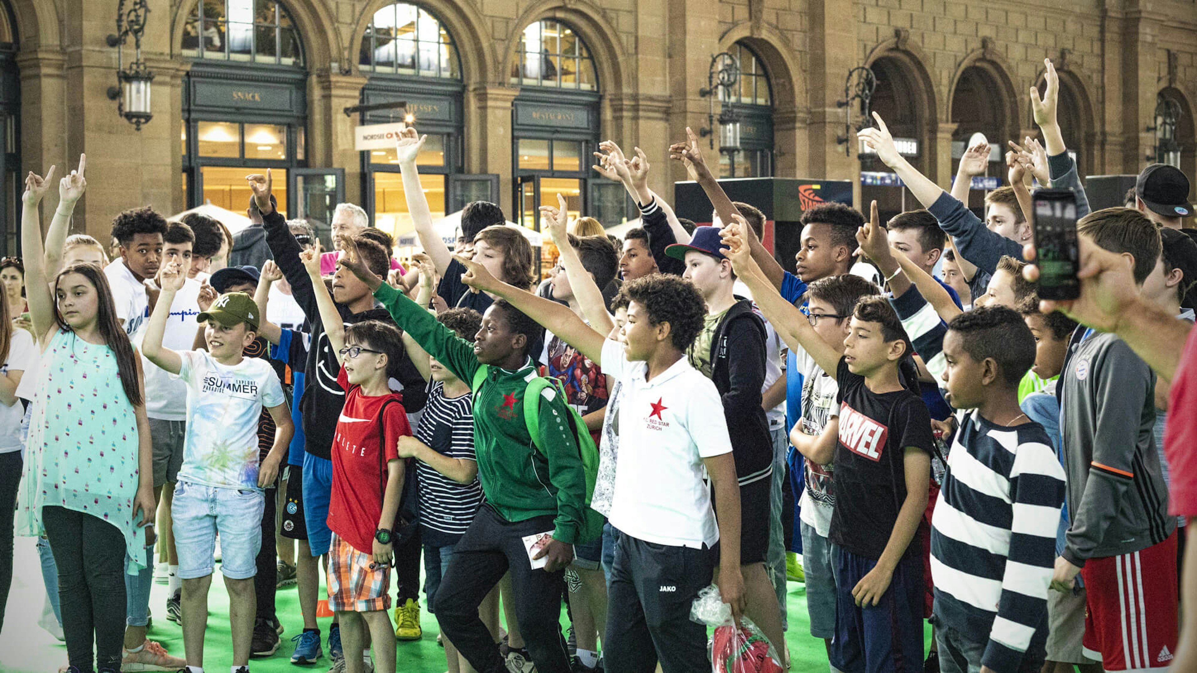 A group of excited children raising their hands during an event at Panini Stadion Zürich.