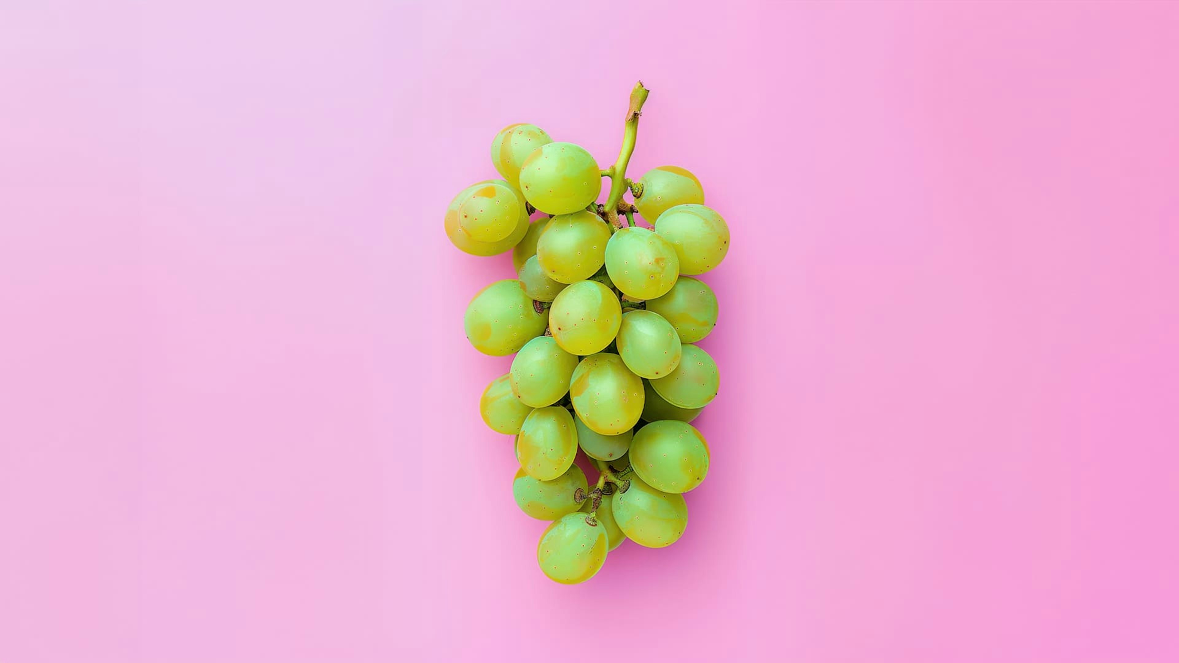 Primo piano di un grappolo di uva verde brillante, disposto su uno sfondo rosa uniforme.