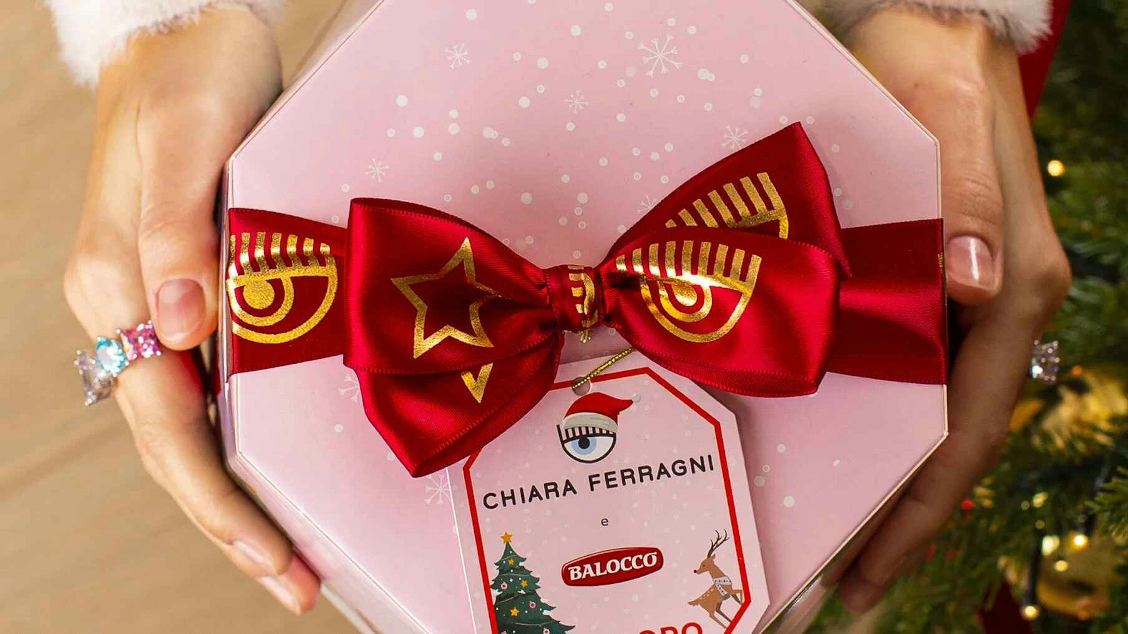 Close-up of a pink Pandoro gift box with a red bow featuring gold designs and a tag reading 'Chiara Ferragni e Balocco,' highlighting a festive collaboration.