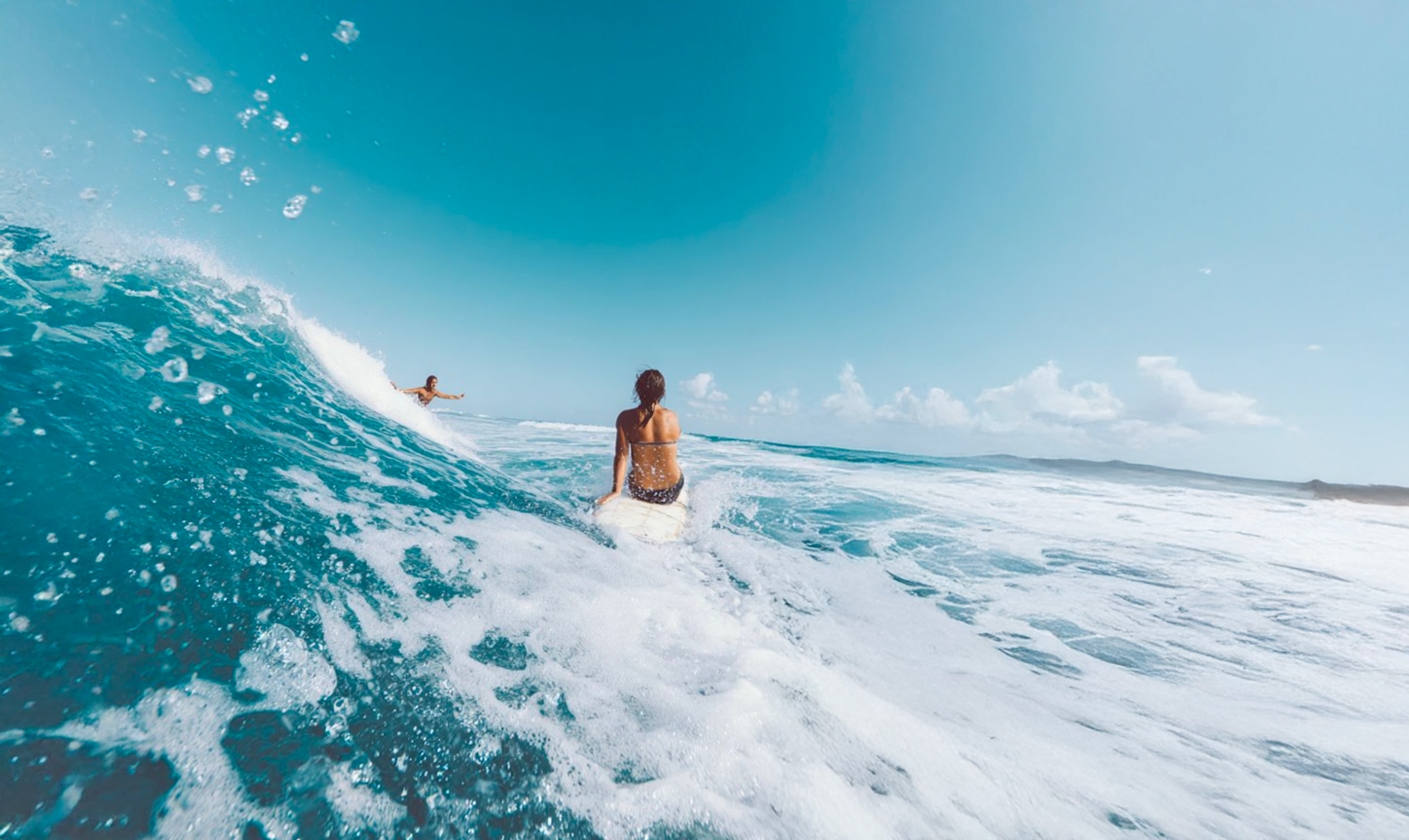 Ragazzi al mare che si divertono, travolti dalle onde con mare cristallino