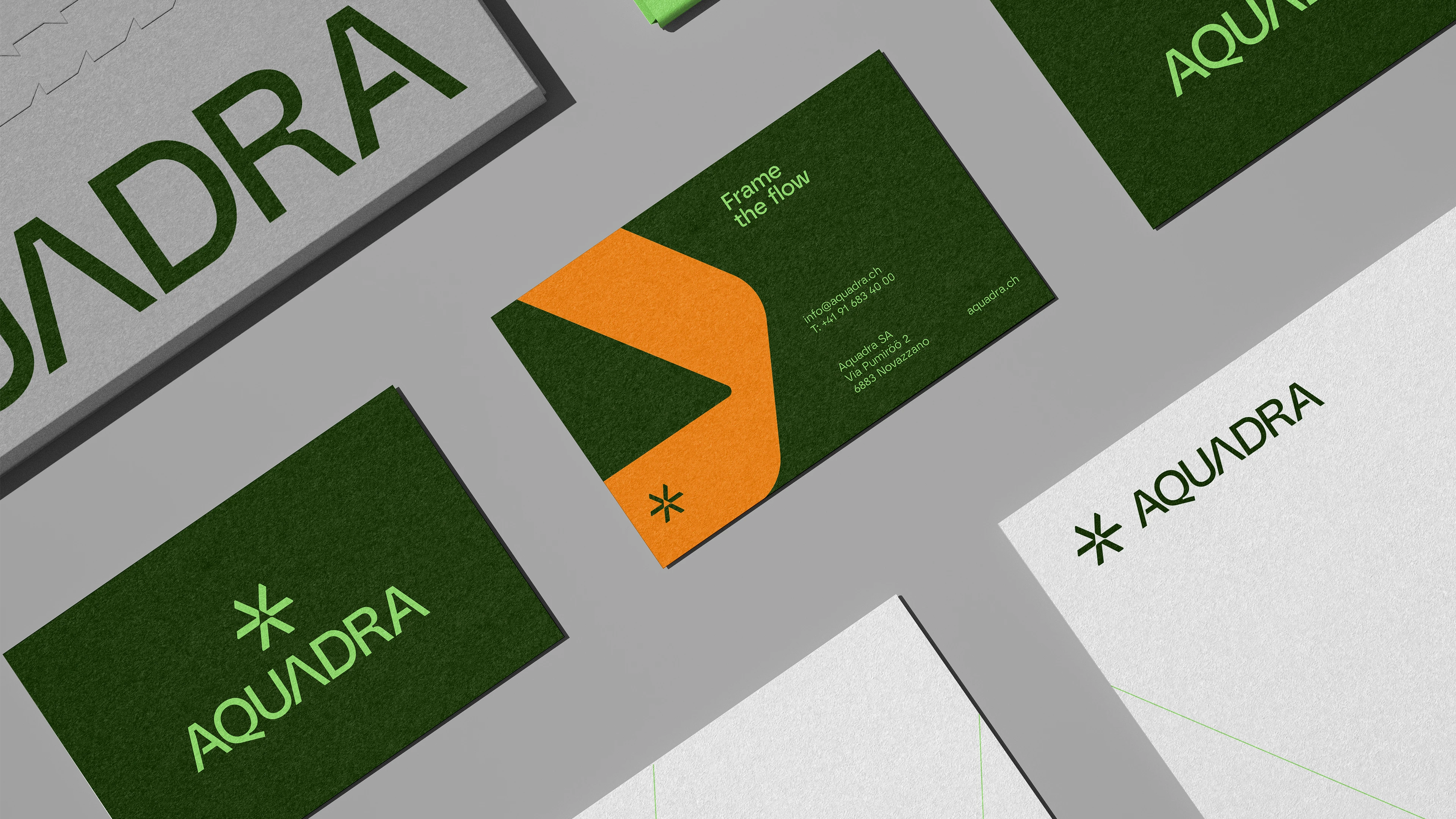 Aquadra's brand featuring business cards and a letterhead. Colors are vibrant green with a distinctive orange fold, displaying the logo & slogan "Frame the flow" emphasizing a modern and eco-friendly brand identity. Alongside contact information.