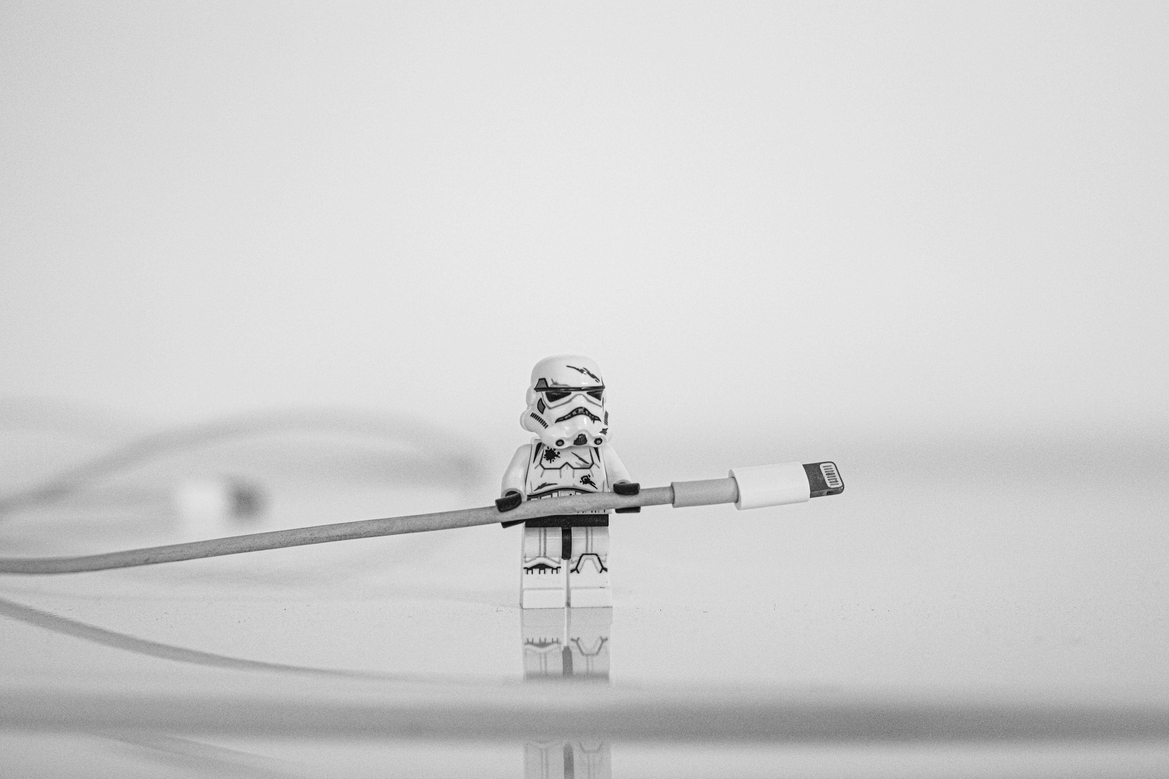 LEGO Star Wars Stormtrooper holding a large charging cable in a minimalist, black-and-white scene.
